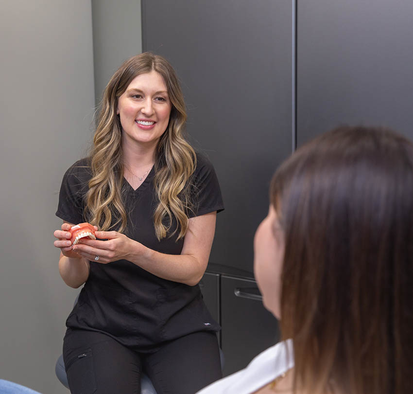 Dental professional explaining oral health using a teeth model during a patient consultation at Boulder Dental Designs in Boulder, CO